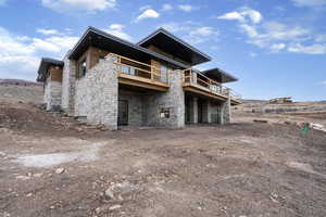 Rear view of property featuring stone siding, a patio area, and a deck