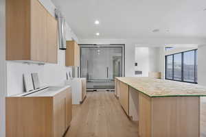 Kitchen featuring light wood finish cabinets, modern cabinets, light wood-style floors, light stone counters, and a center island