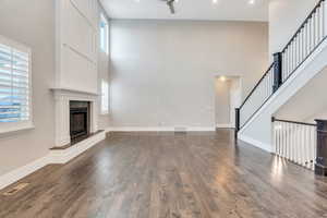 Unfurnished living room with a high ceiling, dark wood-style floors, a fireplace, and healthy amount of natural light