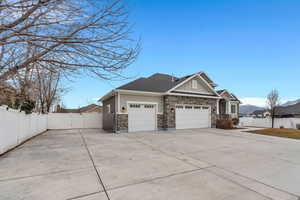 View of side of home featuring driveway, board and batten siding, a gate, an attached garage, and stone siding