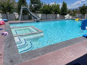 Integrated pool / hot tub featuring a water slide, a fenced backyard, and a patio area