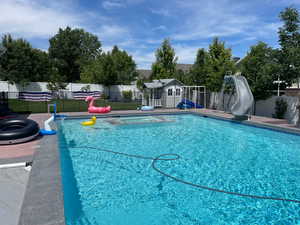 Integrated pool / spa featuring a water slide, a fenced backyard, an outbuilding, and a patio area