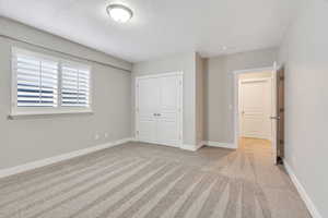 Unfurnished bedroom featuring light carpet, a closet, and a textured ceiling