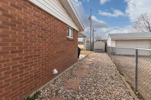 View of property exterior with a fenced backyard, brick siding, a storage unit, and a detached garage