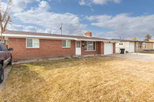 Single story home featuring brick siding, a front yard, a chimney, and concrete driveway