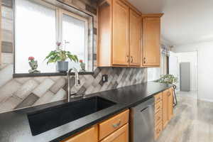 Kitchen featuring stainless steel dishwasher, light wood-style flooring, decorative backsplash, and wood finish cabinetry