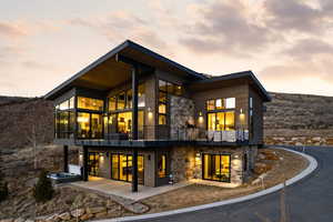 Back of property at dusk with stone siding, a balcony, and a patio