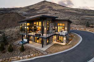 Rear view of house featuring stone siding, a mountain view, a balcony, and an outdoor hot tub