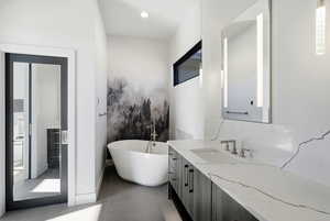 Full bathroom featuring a soaking tub, vanity, dark tile patterned floors, and recessed lighting