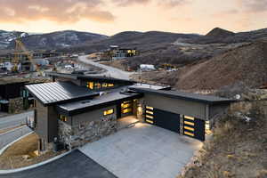 View of front facade featuring a mountain view, concrete driveway, an attached garage, stone siding, and a standing seam roof