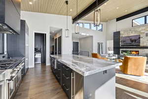 Kitchen with hanging light fixtures, dark cabinetry, stainless steel stove, extractor fan, and dark wood finished floors