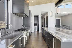 Kitchen with hanging light fixtures, light stone counters, exhaust hood, range with two ovens, and a high wooden beamed ceiling
