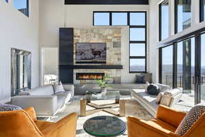 Living area featuring a high ceiling, a stone fireplace, and plenty of natural light