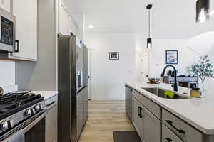 Kitchen featuring stainless steel appliances, light wood-style flooring, decorative light fixtures, light stone countertops, and a center island with sink