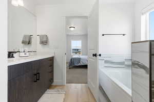 Ensuite bathroom with vanity, a bath, and light wood-style flooring