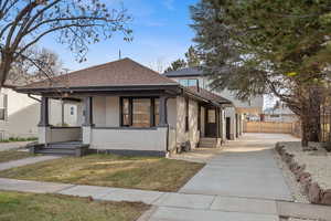 Bungalow-style house with a shingled roof, stucco siding, a porch, and concrete driveway