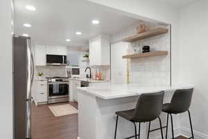 Kitchen featuring open shelves, stainless steel appliances, white cabinets, light stone counters, and tasteful backsplash