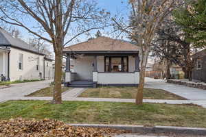 View of front facade with a porch, a shingled roof, a front yard, and stucco siding