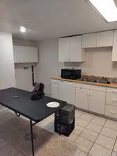 Kitchen featuring white cabinets, dishwasher, black microwave, light countertops, and light tile patterned flooring