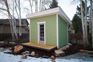 Snow covered structure with a fenced backyard and a storage shed