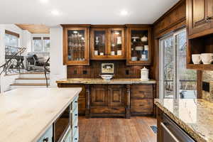 Bar with dark wood finished floors, stainless steel appliances, two tone color scheme, and light stone countertops