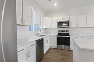 Kitchen featuring stainless steel appliances, white cabinets, dark wood finished floors, light stone counters, and recessed lighting