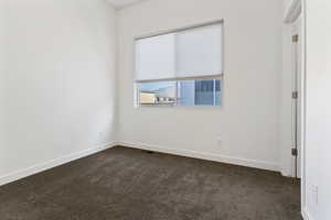 Spare room featuring dark carpet and baseboards