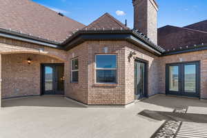 View of exterior entry with french doors, a patio, a chimney, and brick siding