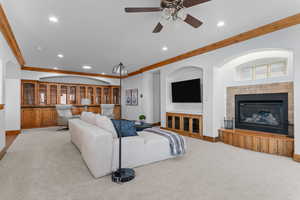 Living room with carpet flooring, recessed lighting, ceiling fan, a fireplace, and crown molding