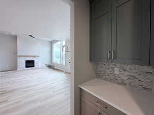 Bar area featuring light wood-type flooring, decorative backsplash, a glass covered fireplace, and light stone countertops