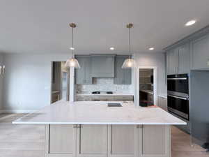 Kitchen with light stone countertops, stainless steel double oven, light wood-style flooring, and gray cabinetry
