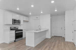 Kitchen featuring a peninsula, stainless steel appliances, white cabinetry, recessed lighting, and light wood finished floors