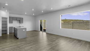 Kitchen with gray cabinets, a center island with sink, recessed lighting, light wood-type flooring, and light stone counters