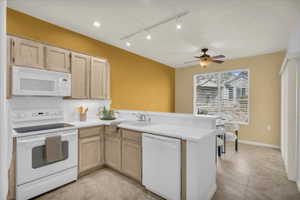 Kitchen with white appliances, light wood finish cabinets, a peninsula, light countertops, and rail lighting