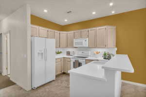 Kitchen with white appliances, light countertops, light wood finish cabinetry, a peninsula, and a breakfast bar
