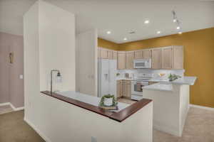 Kitchen with a peninsula, white appliances, recessed lighting, a kitchen bar, and light wood finish cabinetry