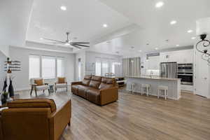 Living area featuring ceiling fan, healthy amount of natural light, light wood-style floors, recessed lighting, and a tray ceiling