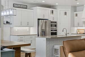Kitchen featuring tasteful backsplash, pendant lighting, stainless steel appliances, and white cabinets