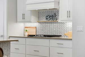 Kitchen with white cabinetry, open shelves, backsplash, and stainless steel gas cooktop
