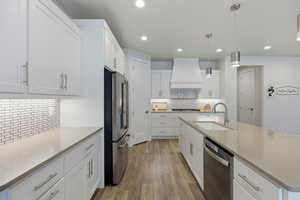 Kitchen featuring hanging light fixtures, white cabinetry, a center island with sink, and stainless steel appliances