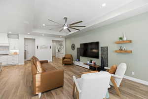 Living room featuring a ceiling fan, recessed lighting, light wood finished floors, and a raised ceiling