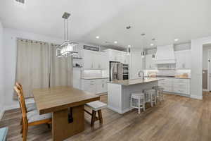 Kitchen with white cabinetry, a kitchen breakfast bar, tasteful backsplash, an island with sink, and hanging light fixtures