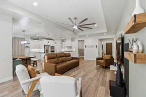 Living area with light wood-style flooring, a ceiling fan, a tray ceiling, and recessed lighting