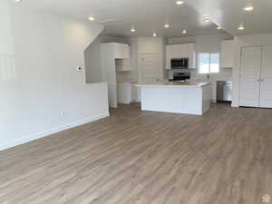 Kitchen featuring white cabinets, light countertops, stainless steel appliances, open floor plan, and light wood finished floors