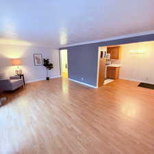 Living room with light wood-style flooring, hanging lights, ornamental molding, and a textured ceiling