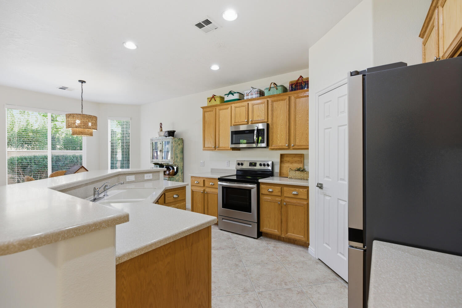 Kitchen featuring stainless steel appliances, decorative light fixtures, a kitchen island with sink, light tile patterned floors, and wood finish cabinetry