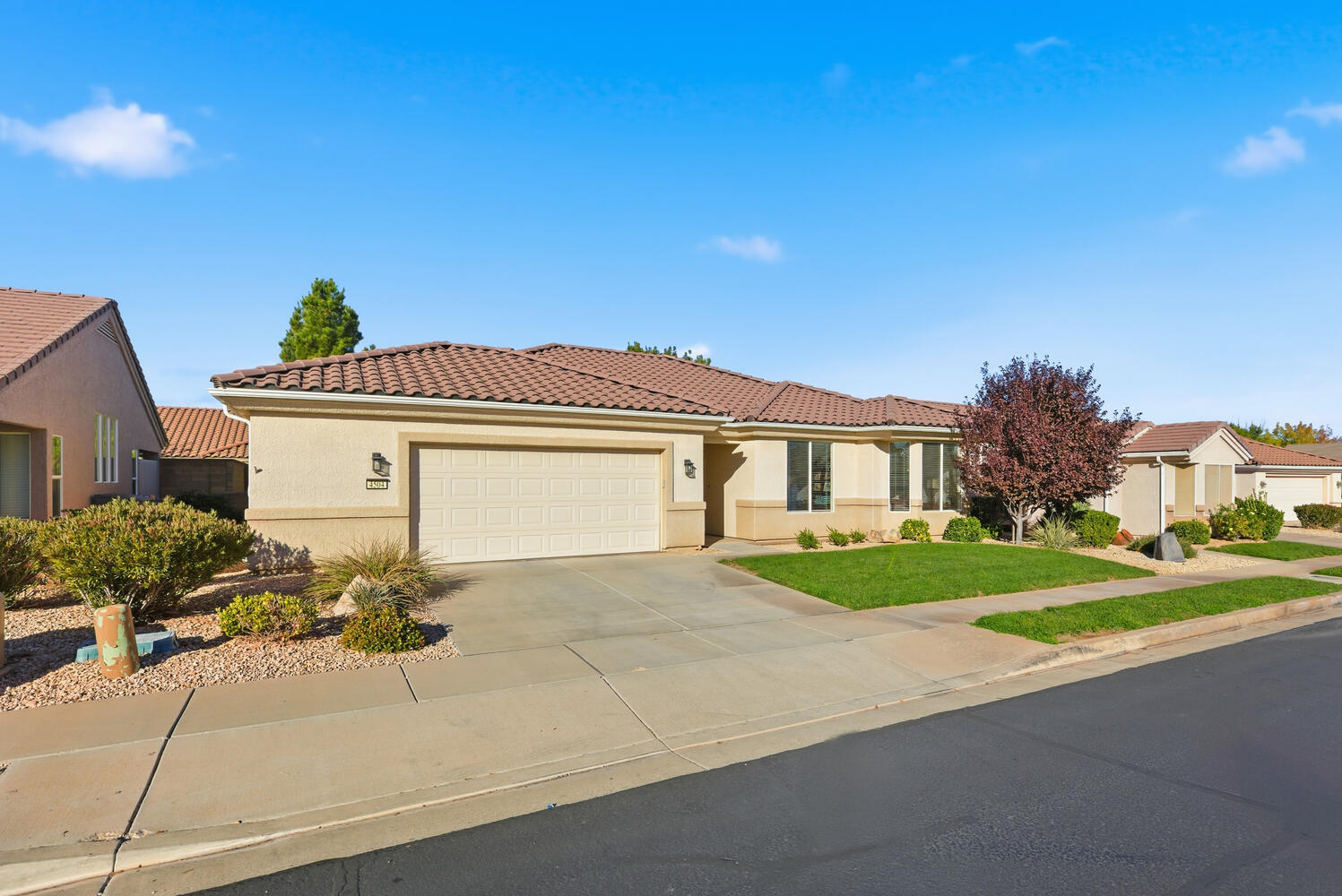 View of front of house with driveway, stucco siding, an attached garage, a tiled roof, and a front yard
