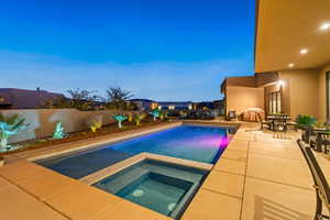 Pool at dusk with outdoor dining space, a patio area, a fenced backyard, and a pool with connected hot tub