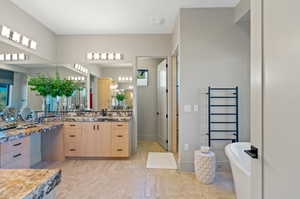 Bathroom with a towel warmer, a soaking tub, and vanity