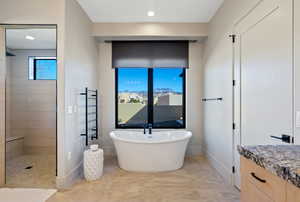Full bathroom featuring walk in shower, a freestanding bath, a towel warmer, and vanity